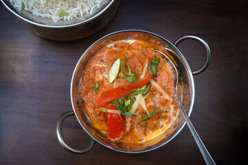 Indian vegetarian curry dish with tomato and spring onions in a stainless steel bowl served with rice on a dark brown wooden table, copy space, high angle view from above