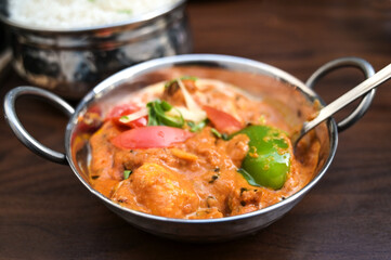 Indian chicken curry dish with vegetables in a steel bowl served with rice on a dark brown wooden table, copy space, selected focus,