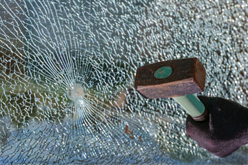 Hand with a hammer and a broken window made of safety glass, concept for burglary and vandalism,...