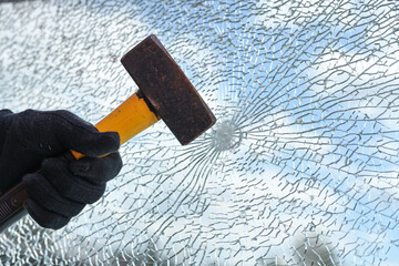 Man’s hand is hitting a window from safety glass with a heavy hammer, vandalism and burglary concept, copy space - 522242799