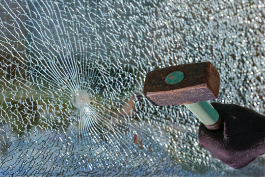 Hand with a hammer and a broken window made of safety glass, concept for burglary and vandalism, copy space