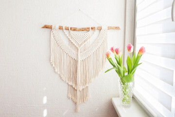 Obraz na płótnie Canvas Handmade macrame. 100% cotton wall decoration with wooden stick hanging on a white wall. Macrame braiding and cotton threads. Female hobby. ECO friendly decoration concept in the interior