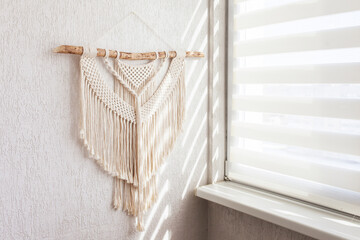 Handmade macrame. 100% cotton wall decoration with wooden stick hanging on a white wall.   Macrame braiding and cotton threads.  Female hobby.  ECO friendly decoration concept in the interior