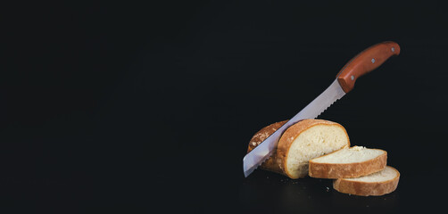 Sliced fresh bread and cutting knife on black background.