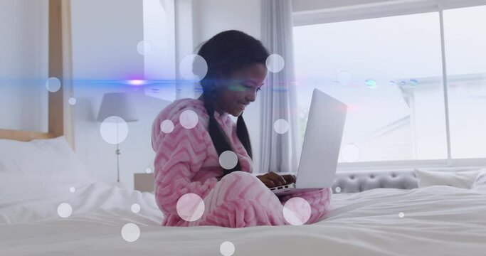 Animation of light spots and trails over african american girl using laptop