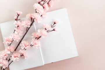White book mockup on a pastel pink background with white and pink cherry blossom. Education, reading. Brochure, magazine, book or catalog mock up isolated. Copy space.