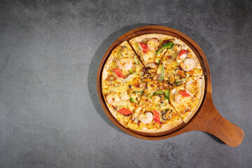 Top view of tasty hot baked seafood crispy pizza - mussels, shrimps and kani with chili pepper and melted mozzarella cheese on round pizza dough, on a wooden pizza pan over concrete texture.