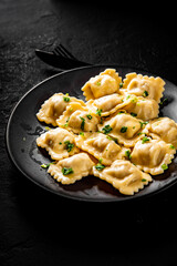 Meat dumplings - russian pelmeni, ravioli with meat in black plate on Dark grey black slate background