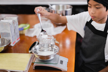 Young boy measuring ingredient for baking in kitchen.