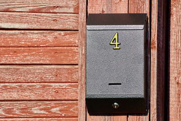 Mailbox with number 4 hanging on wall of wooden house upholstered in red boards.