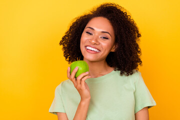 Photo of cheerful positive lady wear green t-shirt eating apple white teeth empty space isolated yellow color background