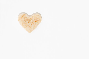 Abstract creative love card made of heart shaped cut-out from slice of white bread standing on isolated pastel white background. Minimal flat lay. High-carb or easily digestible food concept.