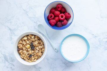 Bowl of homemade granola cereal with greek yogurt and fresh raspberry berries on white marble table background. Top view, flat lay, copy space. Healthy eating concept. 