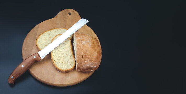A large knife cuts thin pieces of white bread from a rectangular loaf.