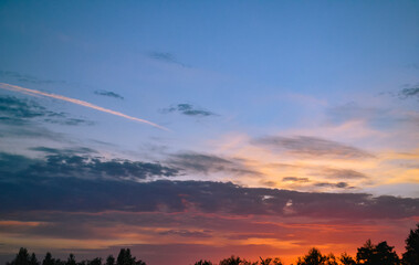 Morning glow illuminates the clouds on a beautiful colorful sky above the silhouettes of trees at dawn