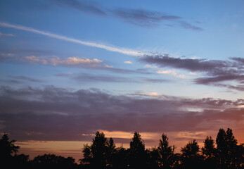 Morning glow illuminates the clouds on a beautiful colorful sky above the silhouettes of trees at dawn