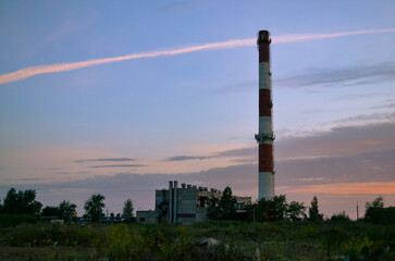 Fototapeta na wymiar Tall chimney of a boiler house against the backdrop of a beautiful morning sky and clouds