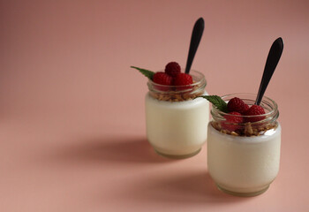 natural white yogurt in a glass jar with raspberries, muesli and metal spoon