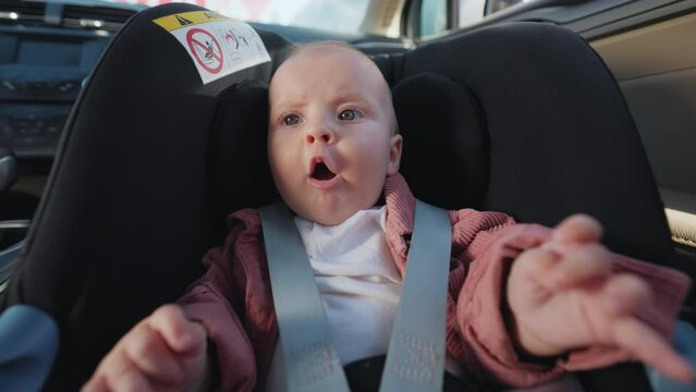 Portrait of cute toddler baby boy with scared face emotions sitting in child seat while travelling by car. Horizontal footage of cute curious toddler in automobile. Vehicle, transport, trip
