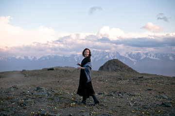 Fototapeta premium High up in the mountains. Walk in the clouds. Meet the sunset at the top of the mountain. A girl in a black dress walks on top of a mountain. North-Chuysky ridge. Wind in the hair. Freedom.
