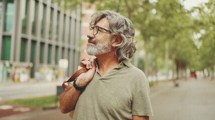 Middle-aged man with gray hair and beard walks and looks around. Mature gentleman in eyeglasses...