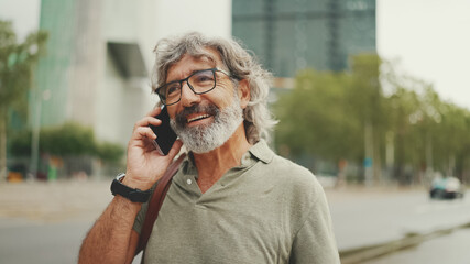 Friendly middle aged man with gray hair and beard wearing casual clothes using his mobile phone....