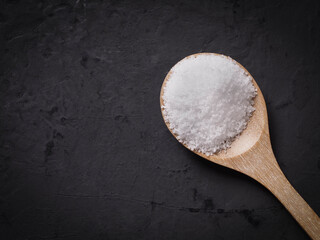Sea ​​salt in a wooden spoon on a black table background.
