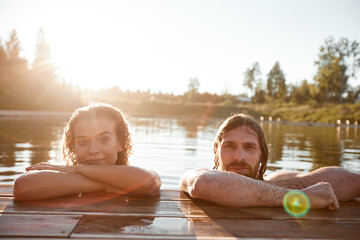 Summer portrait of young couple swimming in lake lit by Sunlight and looking at camera