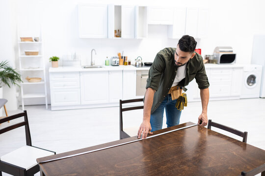 Young arabian carpenter measuring wooden table in kitchen