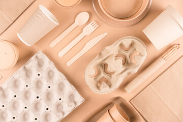 Sustainable paper packaging for food industry - paper utensils, cups, plates, drinking straws, egg boxes and food containers over light brown background. Flat lay. Text ECO. Food delivery service