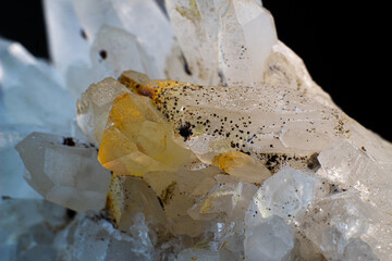 White quartz cluster with yellow and black inclusions on black surface