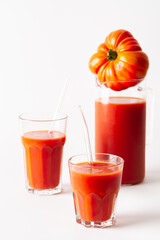Homemade freshly squeezed tomato juice in glasses and a jug with tomatoes on a white background