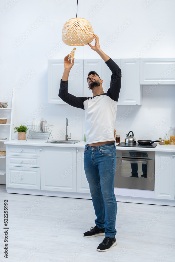 Wall mural Arabian man holding lightbulb near chandelier in kitchen