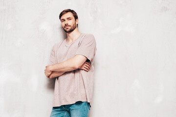 Portrait of handsome smiling stylish hipster lambersexual model. Sexy man dressed in pink T-shirt and jeans. Fashion male isolated on grey wall in studio