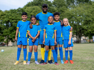 Coach and kids (8-9) posing for group portrait on soccer field