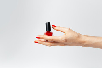 Fototapeta premium Close-up of female hand with red manicure holding a glitter nail polish of red color on white background.