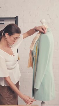 vertical video of designer measuring jacket on mannequin in workshop