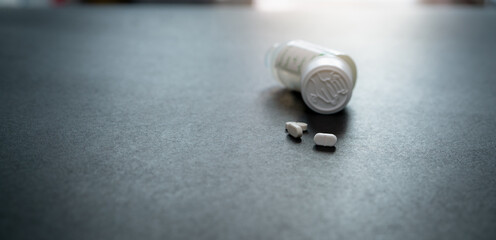 White tablets pills and blur child-resistant pill bottle on black table. Prescription drugs....