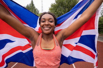 Fototapeta premium Portrait of smiling athletic�woman with British flag on running track