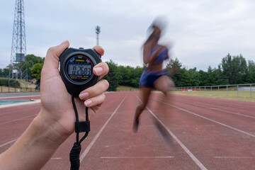 Athletic woman�running on track, hand holding stopwatch in foreground