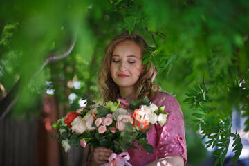 Naklejka premium Young happy blonde woman in a pink dress with a large bouquet of flowers walks around the old European city and enjoys life on a summer day, beautiful portraits with a huge bouquet of flowers.