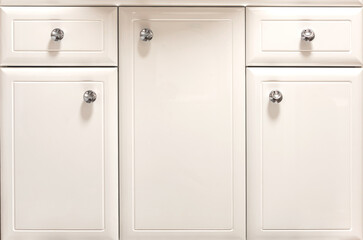 White facade of modern bathroom furniture with doors and drawers with chrome handles.