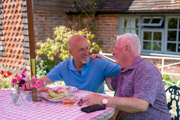 Senior male couple having fruit snack and drinks in garden