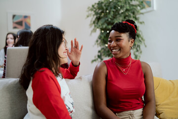 Friends, sisters, cousins meet on Christmas Eve and Christmas Day at home for dinner, women sit on the couch and talk, gossip, laugh, in the background the family sits at the table