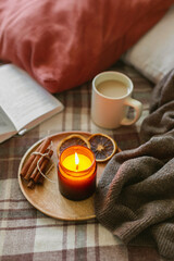 Burning candle with wooden wich in amber glass gar, open book and cup of coffee or tea. Autumn home decor.