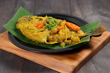 Ikan Gurami Pesmol or Pesmol Fish with Yellow Curry, Close Up on Wooden Table.