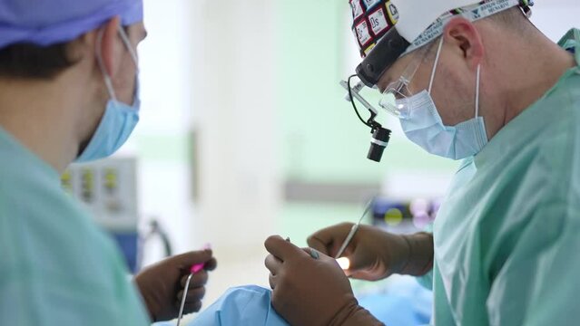 Nasal operation conducted by two doctors. Surgeon using metal tools in the patient’s nose. Blurred backdrop.
