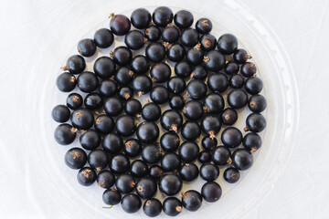 Black berries on white. Blackcurrants in a transparent bowl isolated on a white background. Blackcurrant with copy space for text. Top view berries closeup.