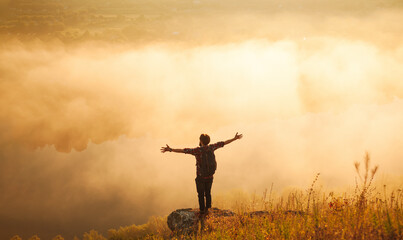 male hiker standing on mountain slope with outstretched arms at sunrise