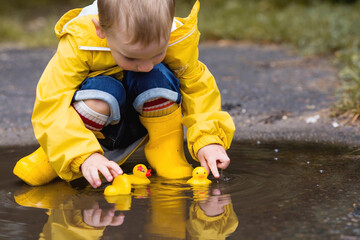 A small child in rainbow socks, yellow rubber boots and a jacket jumps through puddles and plays...
